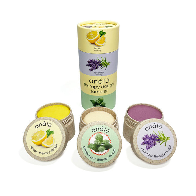 A collection of Analu therapy dough samplers in various colors, with labels indicating flavors such as lemon, lavender, and peppermint. The products are presented in a cylindrical container with a decorative design.