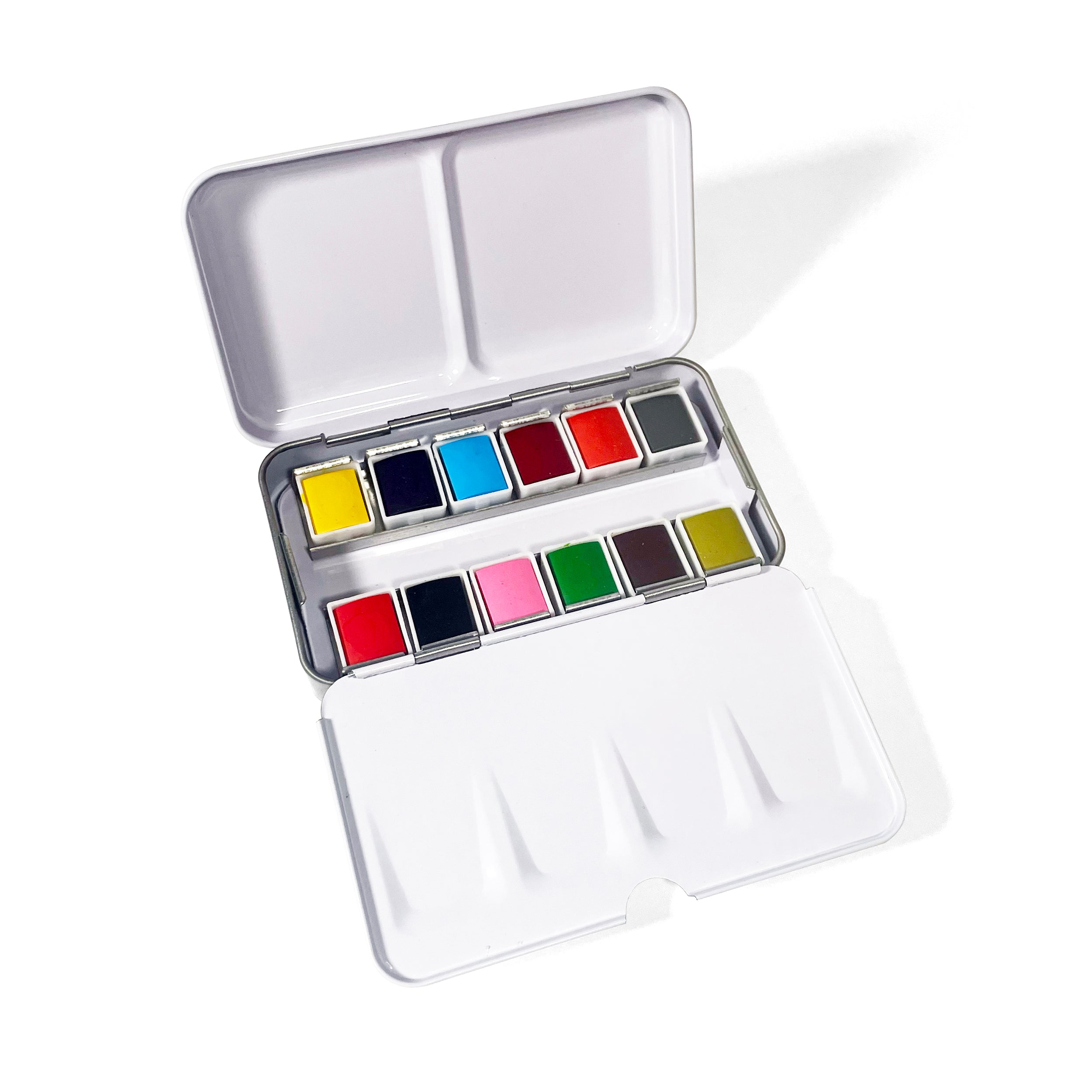 Elseware Unplug Watercolor Set in an open aluminum travel case. The set includes 12 vibrant solid watercolor pans arranged neatly inside, with a built-in mixing area on the lid. Colors range from bright yellows, reds, and blues to deep greens, pinks, and earth tones, providing a versatile palette for artists of all skill levels. This eco-friendly, portable watercolor kit is designed for creativity on the go
