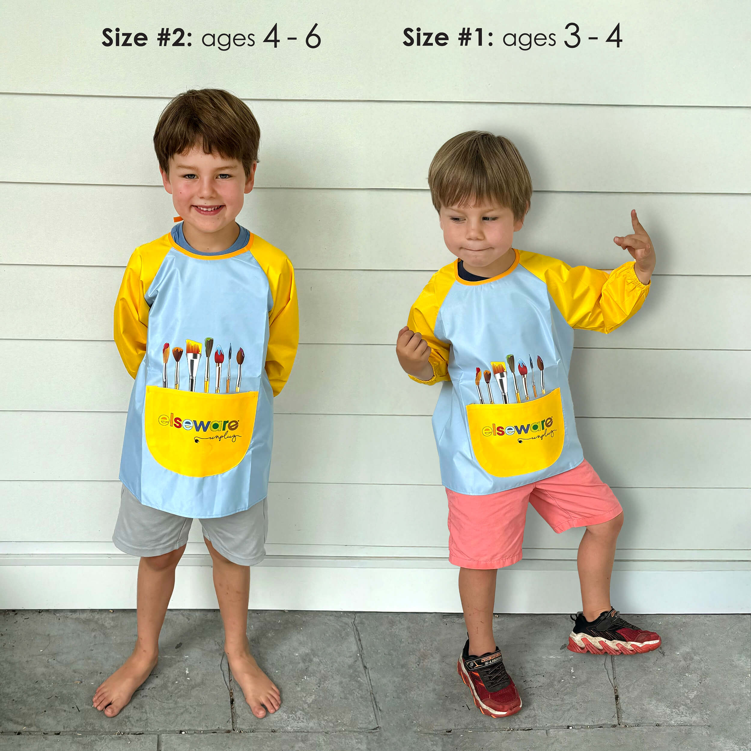 Two children wearing matching Elseware Unplug smocks
with paintbrush pockets against a wooden background.