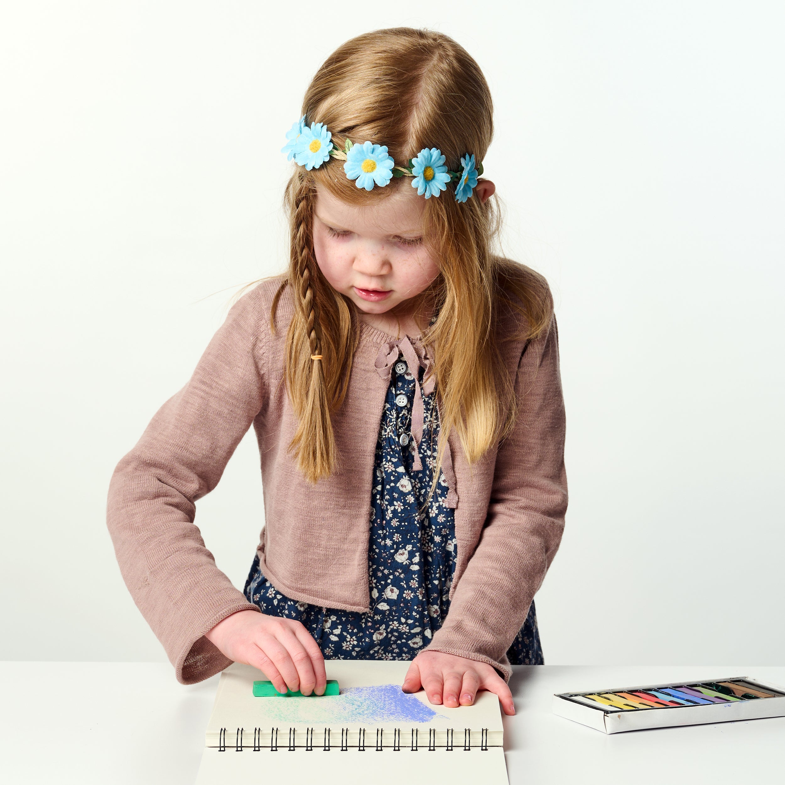 Young girl with a flower headband playing with colorful elsware unplug pastel sticks on a white background