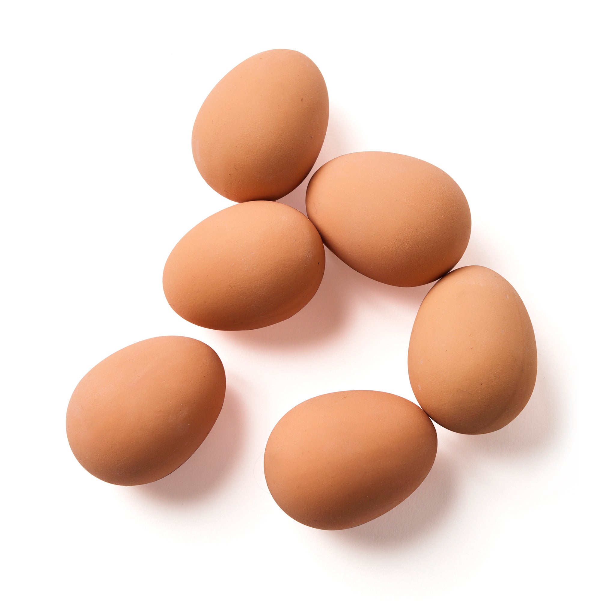 Close-up of six brown rubber bouncy eggs scattered on a white surface, resembling real eggs in size and shape.