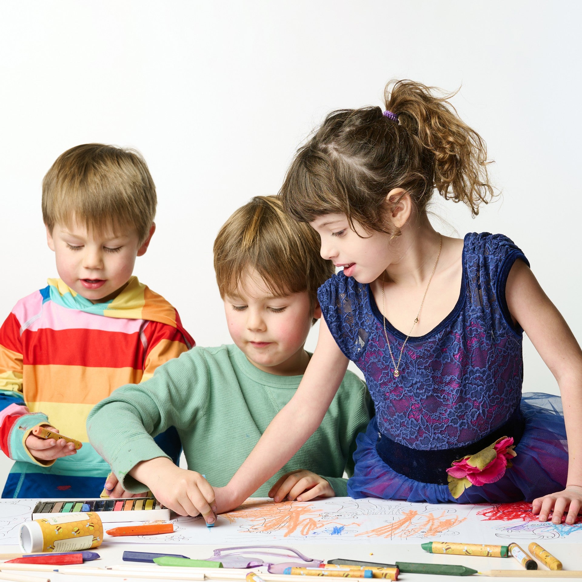 Three young children joyfully coloring on an Elseware Unplug Coloring Scroll using vibrant, non-toxic beeswax crayons and pastels. This eco-friendly, oversized paper roll provides an engaging, hands-on creative experience for collaborative art and imaginative play