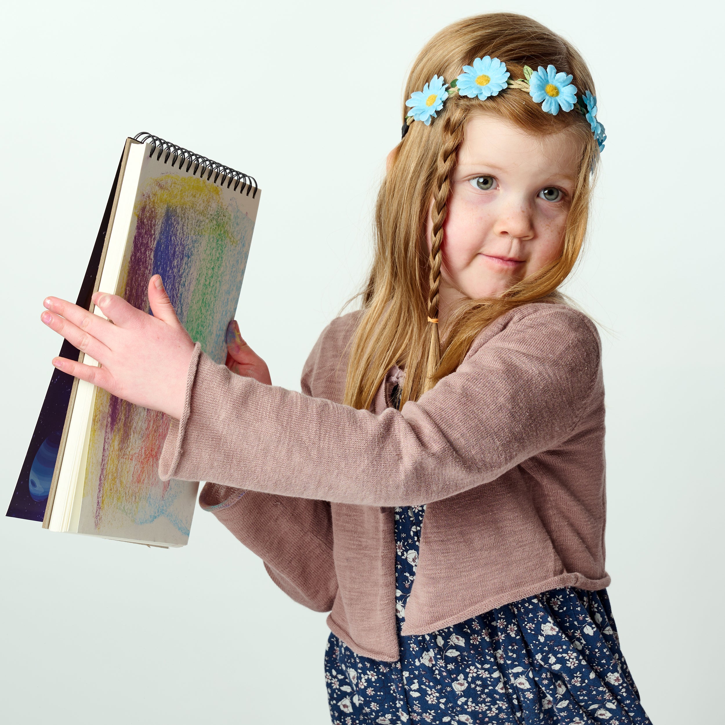 Young girl with braided hair and flower headband holding a colorful elseware unplug art pad against a white background