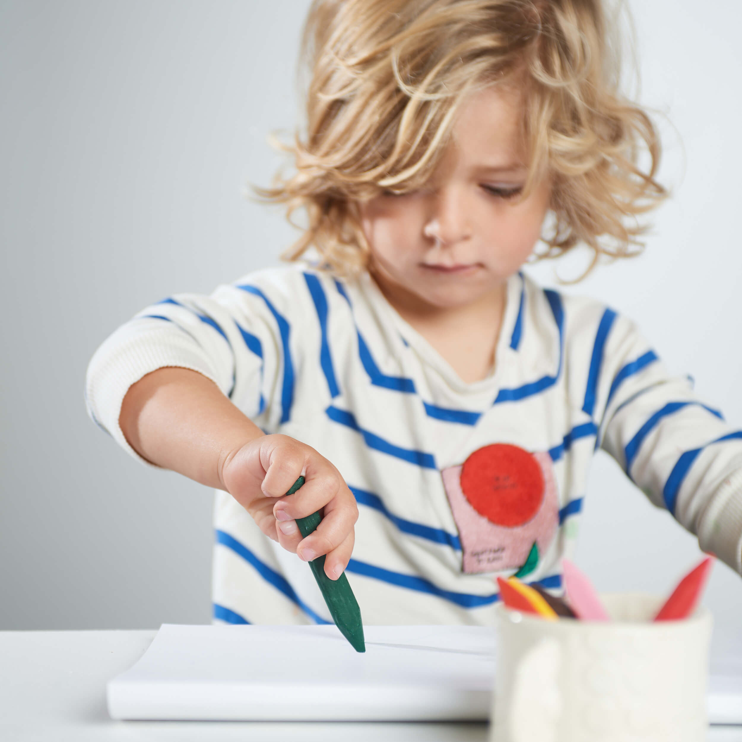 Child drawing with a green crayon on a white surface