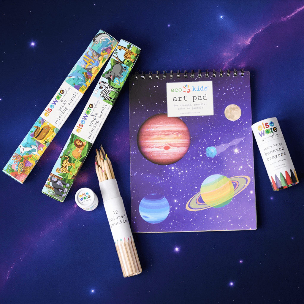 Children's art supplies including an art pad with space-themed design, colored pencils, and beeswax crayons on a cosmic background.