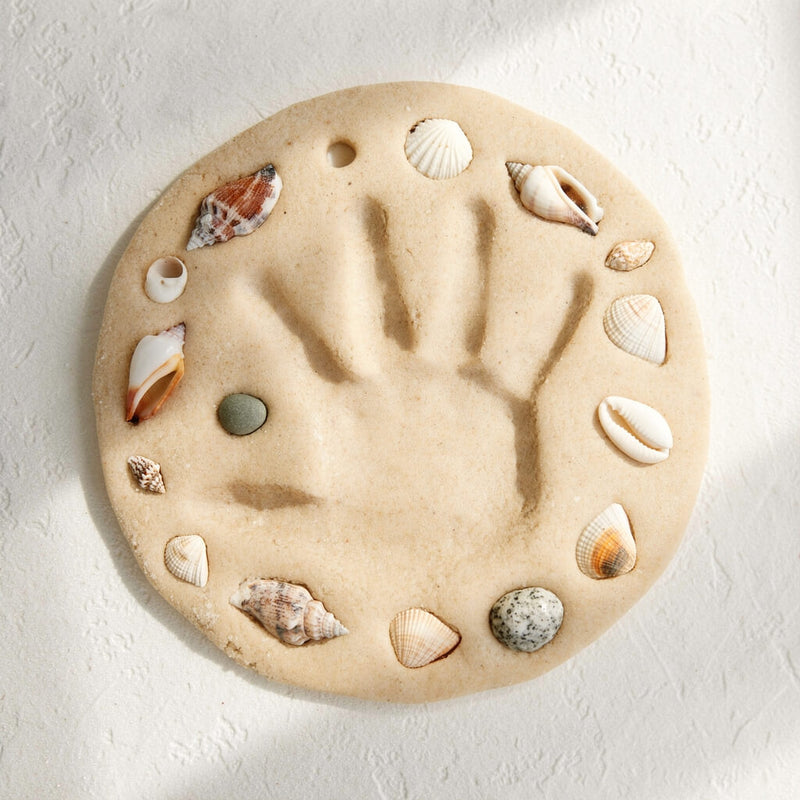 Handprint made of sand with seashells on a light background