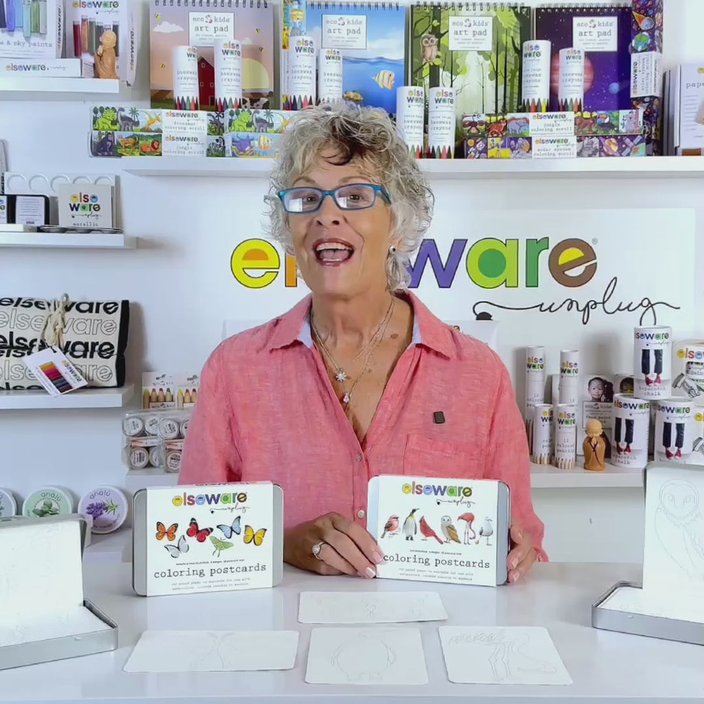 Product demo video showing coloring postcards on textured watercolor paper being decorated with watercolor paint, colored pencils, and markers, and stored in the reusable silver tin.
