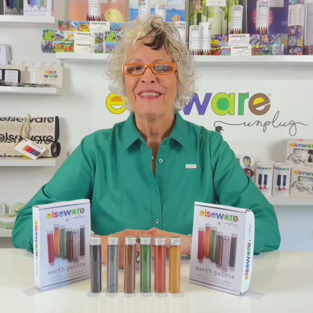 Wisdom Granny in a green shirt from Elseware Unplug demonstrating how to use earth paints with branded Elseware Unplug products displayed in the background.