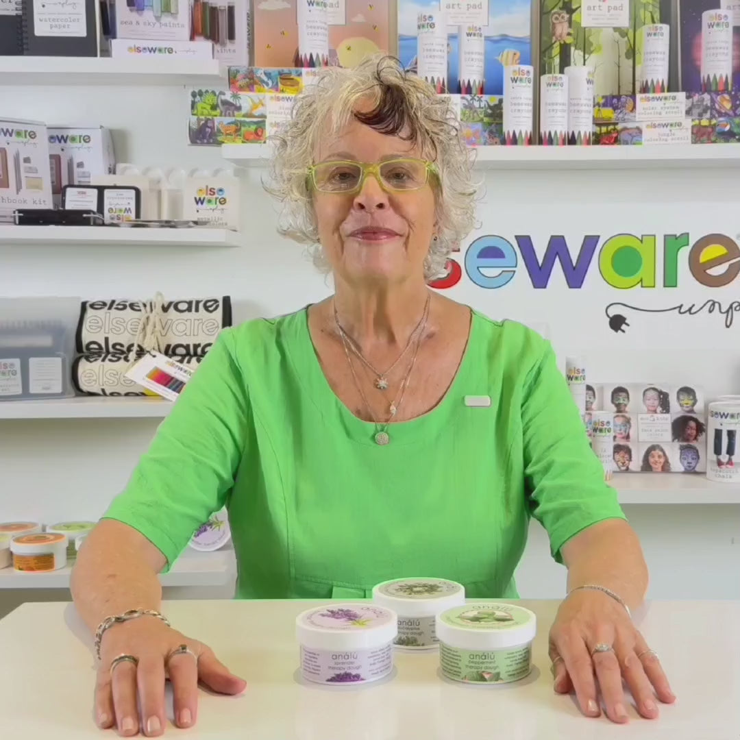 Wisdom Granny in a green shirt from Elseware Unplug demonstrating how to use therapy dough with branded Elseware Unplug products displayed in the background.