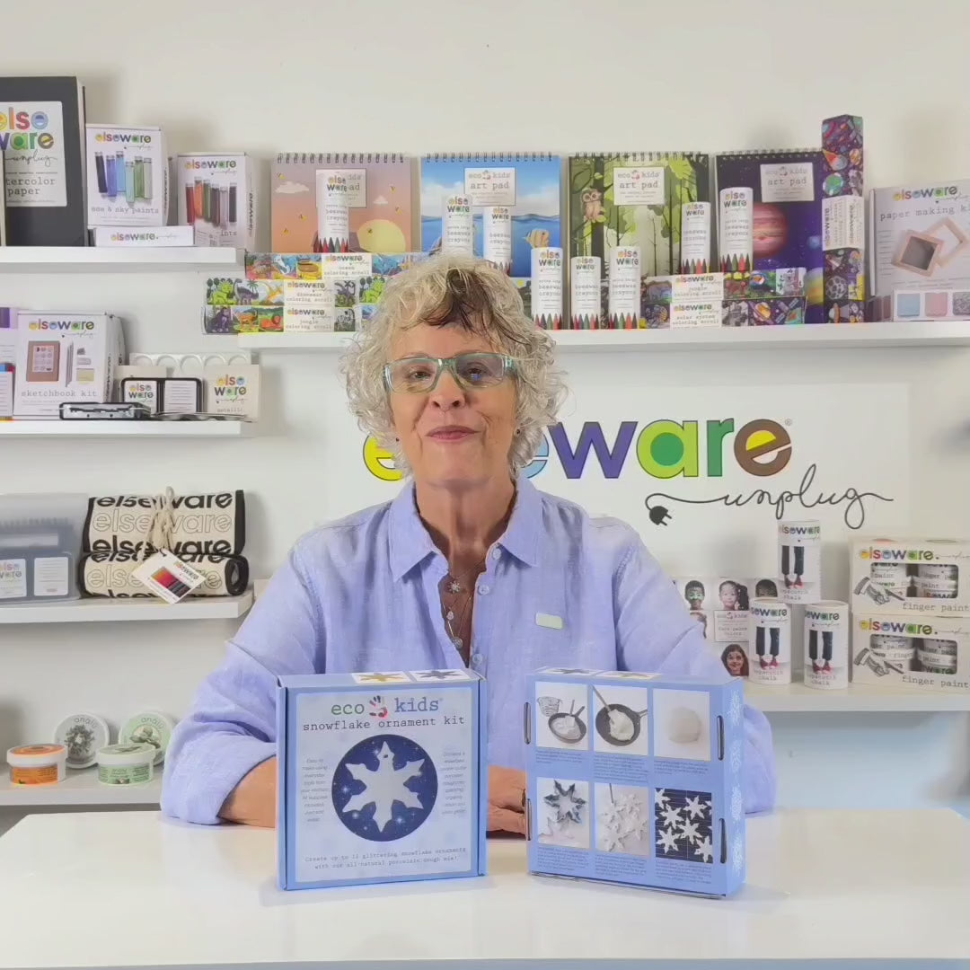 Wisdom Granny in a green shirt from Elseware Unplug demonstrating how to use a snowflake ornament kit with branded Elseware Unplug products displayed in the background.