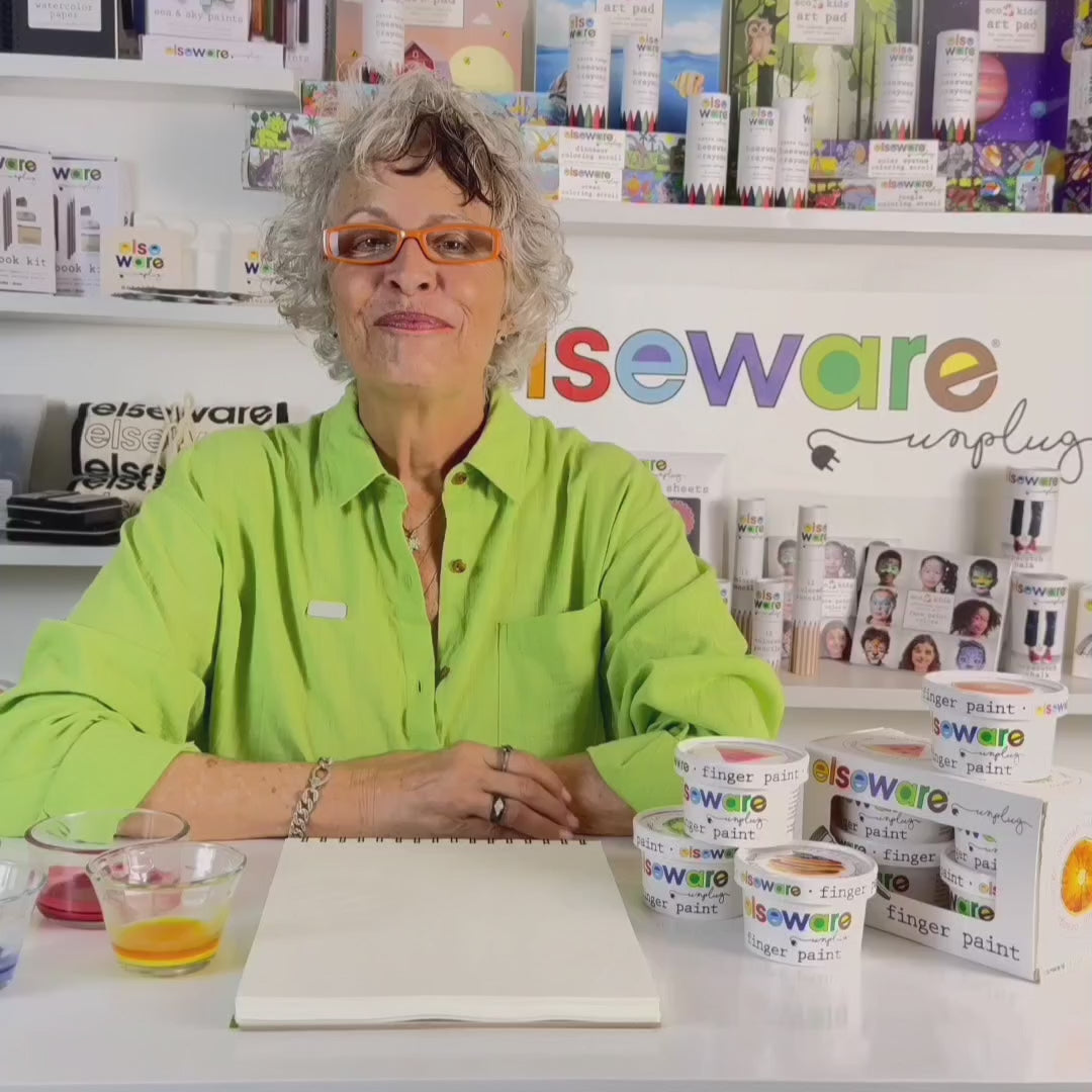Wisdom Granny in a green shirt from Elseware Unplug demonstrating how to use all-natural finger paints on a coloring pad, with branded Elseware Unplug products displayed in the background.